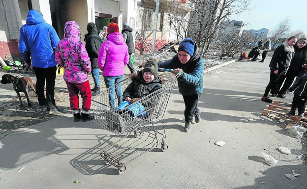 Un niño transporta a su hermano pequeño en un carrito de compra por una de las calles de la asediada Mariúpol. 