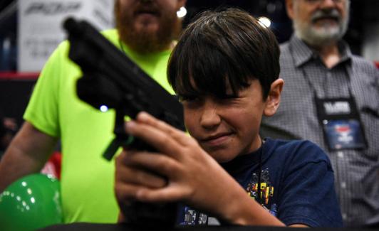 Un niño prueba con un arma electrónica en un juego de puntería virtual durante la convención de la Asociación Nacional del Rifle