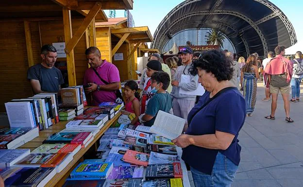 Una lectora consulta un libro en un stand, con la Carpa de Letras al fondo. 