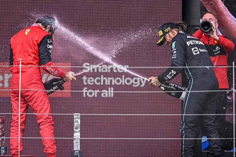 Carlos Sainz y Lewis Hamilton se lanzan champagne sobre el podio.