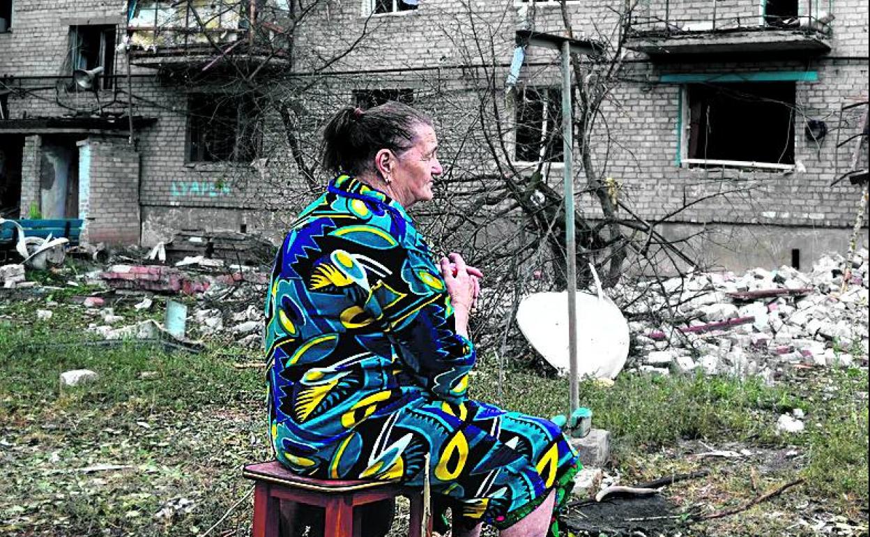 Una mujer se sienta frente a las ruinas de un edificio en Chasiv Ya.