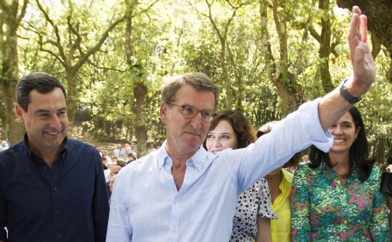 Feijóo, con Juanma Moreno e Isabel Díaz Ayuso a su espalda, saluda a los asistentes al acto del PP. 
