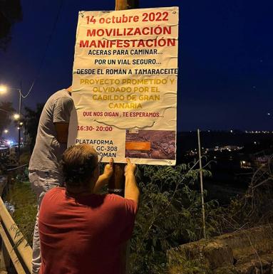 Dos vecinos colocan los carteles en los que se convoca la manifestación. 
