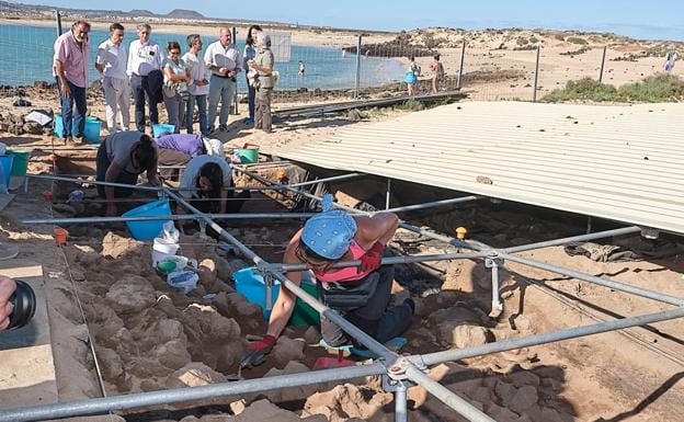 Los arqueólogos trabajan en el yacimiento Lobos I mientras la catedrática Carmina del Arco explica las particularidades de esta campaña a las autoridades del Cabildo de Fuerteventura y de Museos de Tenerife. Bajo las planchas metálicas, están tapados los seis recintos en forma de L y los seis concheros descubiertos en las seis campañas anteriores. 