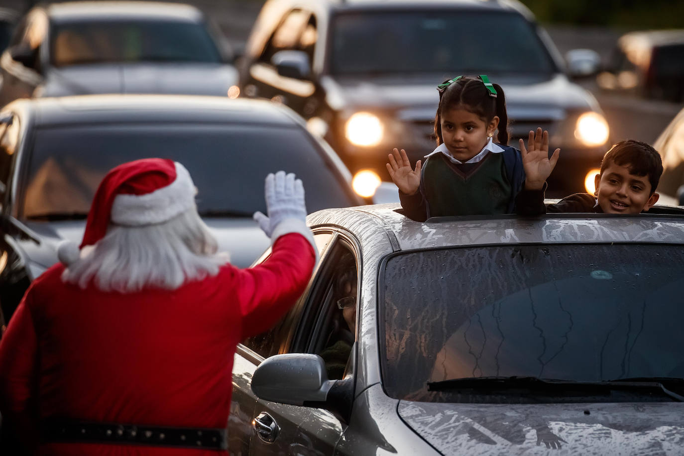 Un hombre vestido de Papá Noel que saluda a unos niños en una autopista con motivo de la llegada del mes de la Navidad en Caracas, Venezuela. 