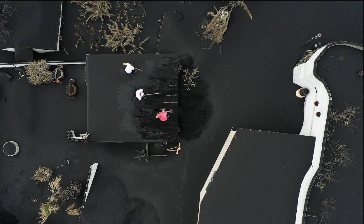 Un grupo de personas retiran las cenizas del tejado de una vivienda en Las Manchas. 