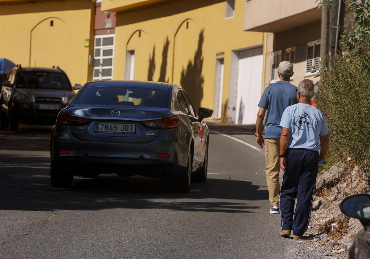 Dos vecinos caminan por una carretera sin aceras en la capital grancanaria.