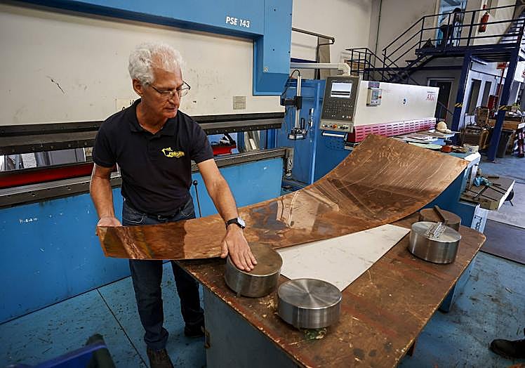 Imagen principal - Juan Carlos García muestra una de las planchas nuevas que creó el taller, a modo de prueba. Debajo, muestrario de las piezas de bronce que sujetan los cristales del faro. Y al lado, esfera de cobre que va sobre la cúpula y que sirve de agarre a la veleta. 