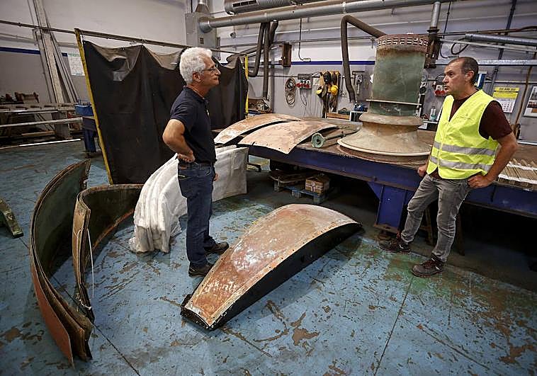 Juan Carlos García y Nicolás Vega dialogan en el taller. En el suelo, varias de las chapas que serán rehabilitadas.