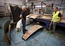 Juan Carlos García y Nicolás Vega dialogan en el taller. En el suelo, varias de las chapas que serán rehabilitadas.