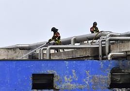 Dos bomberos refrigeran el edificio incendiado.