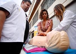 Una sanitaria enseñando a una mujer cómo realizar la maniobra de reanimación.