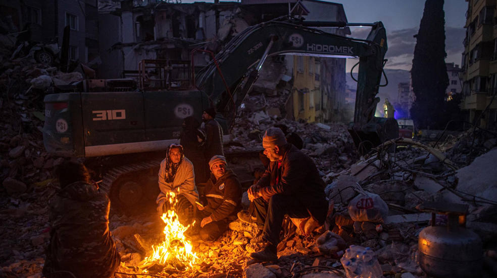 Familiares se sientan alrededor del fuego esperando el cuerpo de un familiar en el lugar de los edificios derrumbados tras un fuerte terremoto, en Hatay, Turquía, el 15 de febrero de 2023. Más de 41.000 personas han muerto y miles más están heridos después de que dos grandes terremotos azotaran el sur de Turquía y el norte de Siria. 