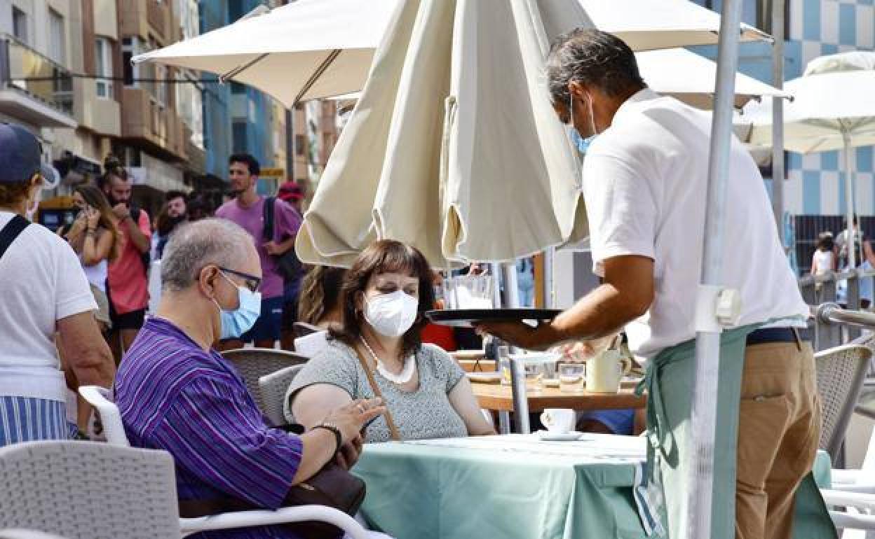Un camarero atiende a dos clientes en Las Canteras. 