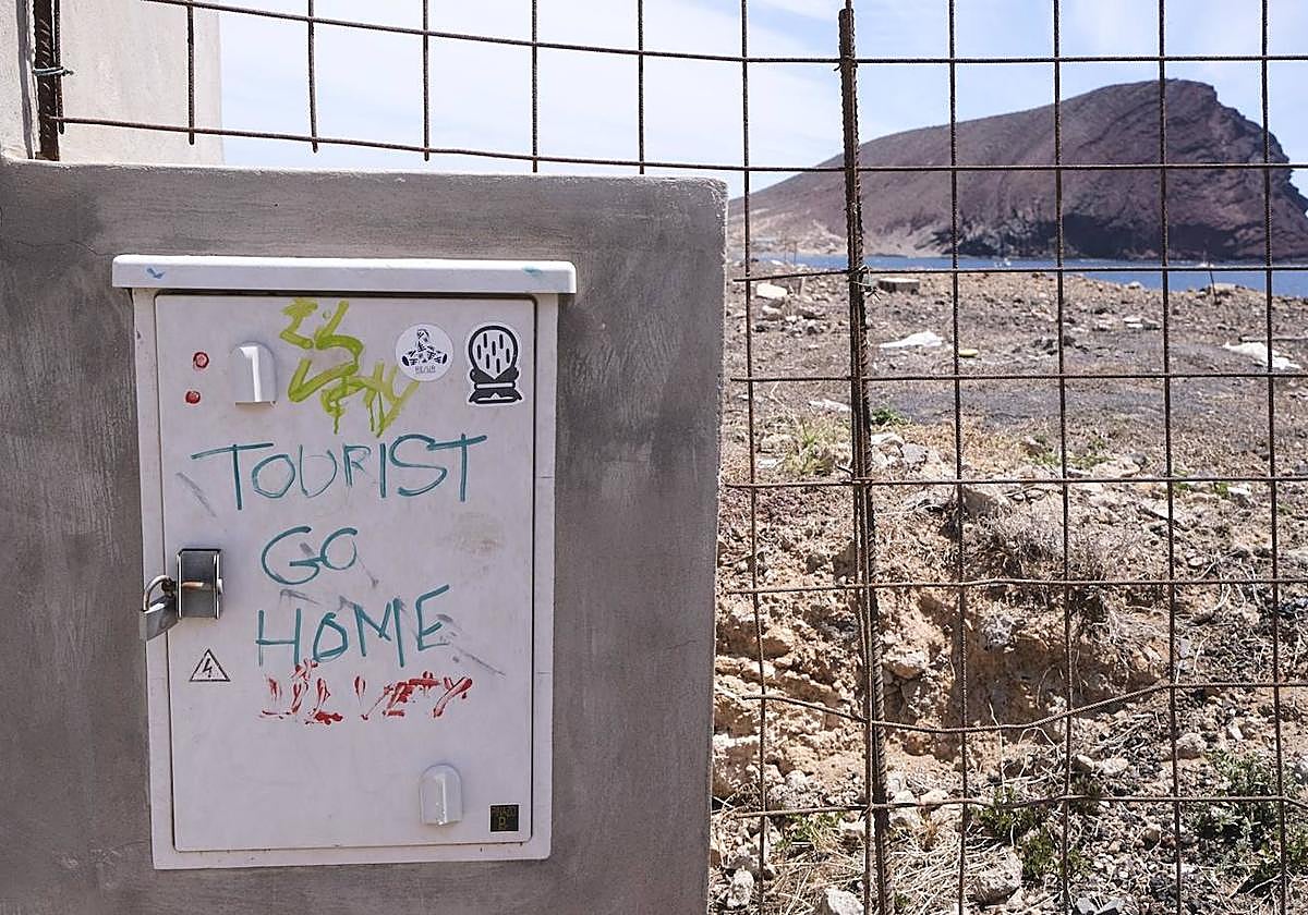 Pintada contra el turismo la valla que rodea las obras de construcción de un hotel en la playa de La Tejita.