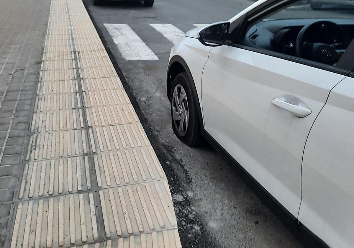 Un coche con el neumático rajado por el filo de la acera, esta semana.