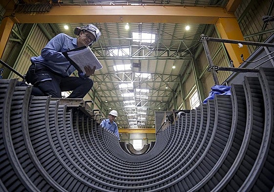 Dos operarios trabajan en la parte del grupo donde va instalada la turbina, también desmontada en otra parte de la nave.