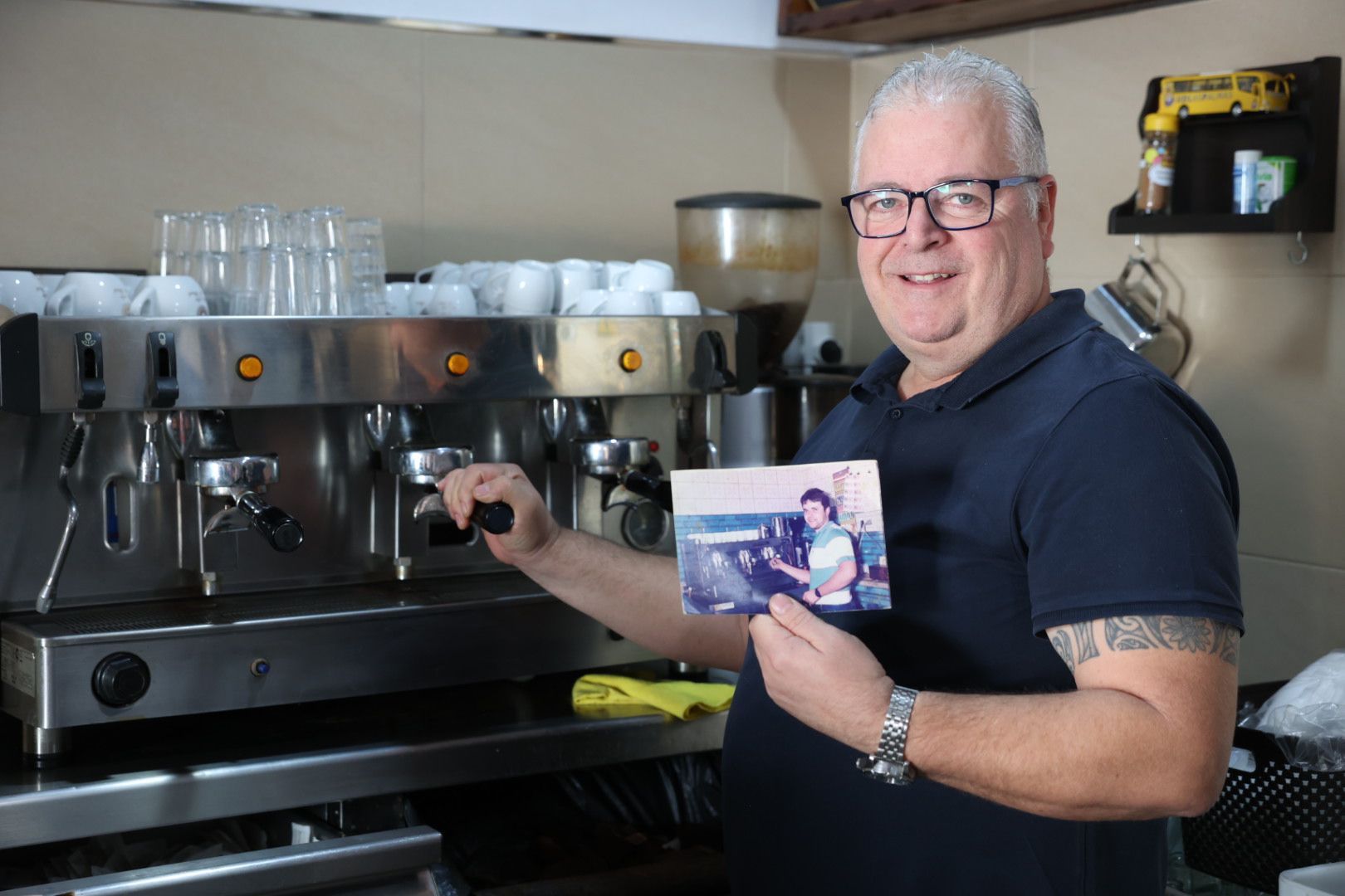 Luis Carlos Pérez, preparando un café, posa con una foto suya de hace más de 30 años en el mismo lugar.