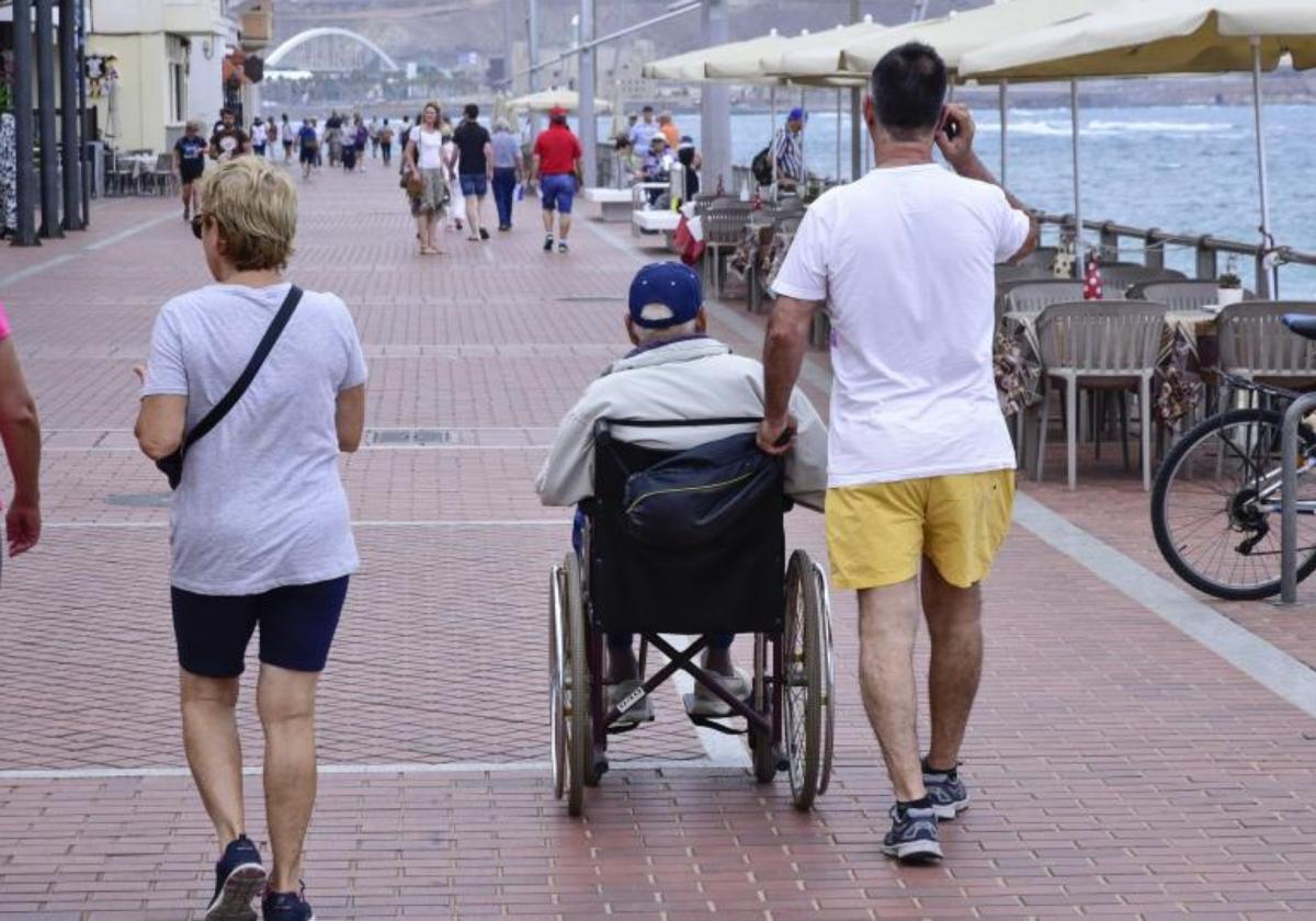 Un hombre camina junto a una persona dependiente por el paseo de Las Canteras.