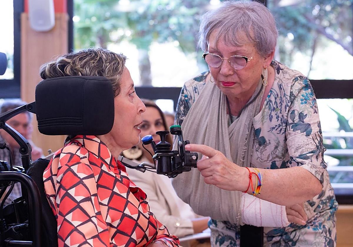 Imagen principal - Arriba, Paqui Domínguez ayuda a Loly durante el acto. Debajo, los músicos Germán López y José Artiles. Y libro firmado por un beso de Loly hecho sello.