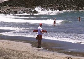 Un socorrista observa a dos bañistas en el agua, en una playa con oleaje y fuertes corrientes.