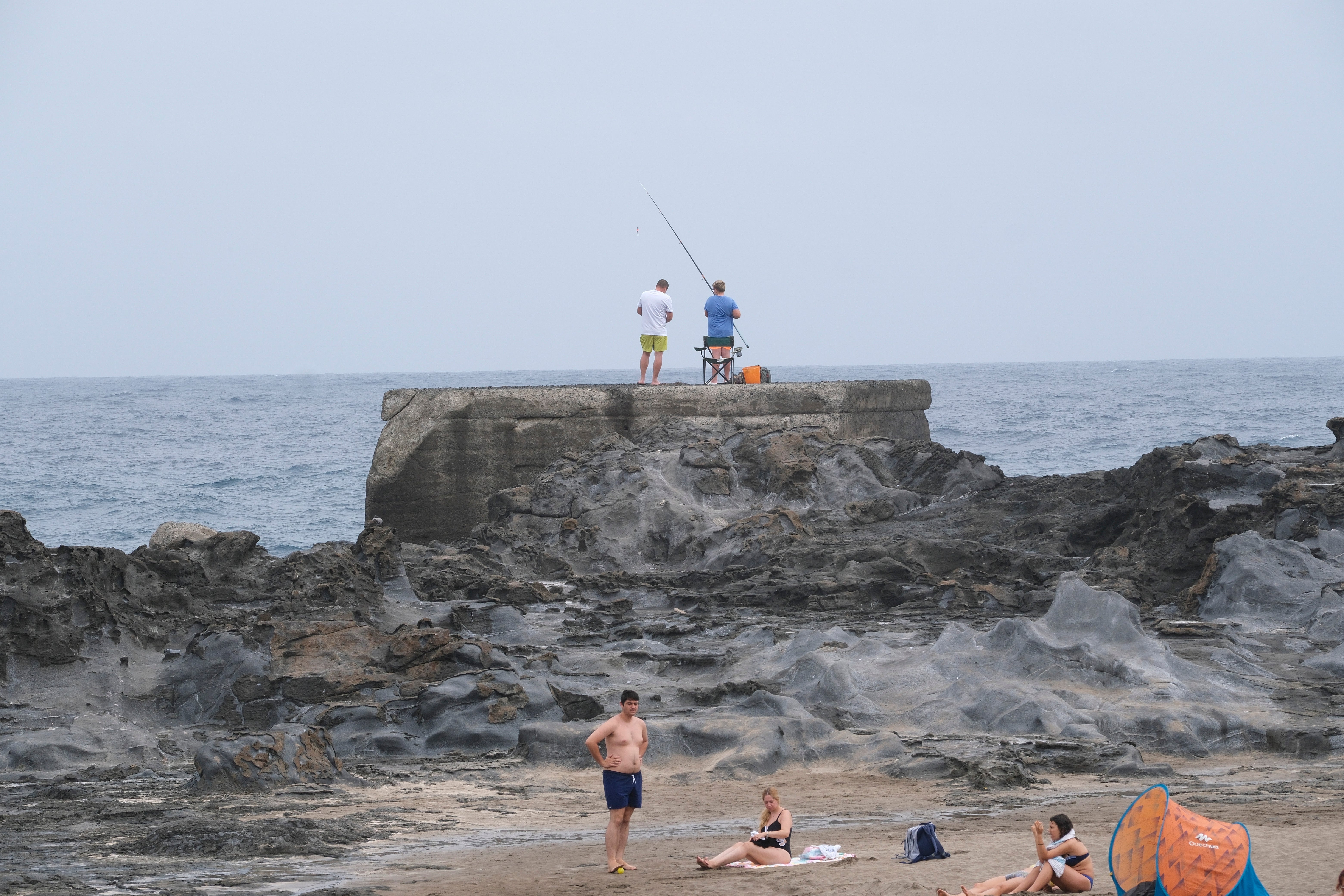 Dos hombres pescando en lo alto de una roca en la playa.