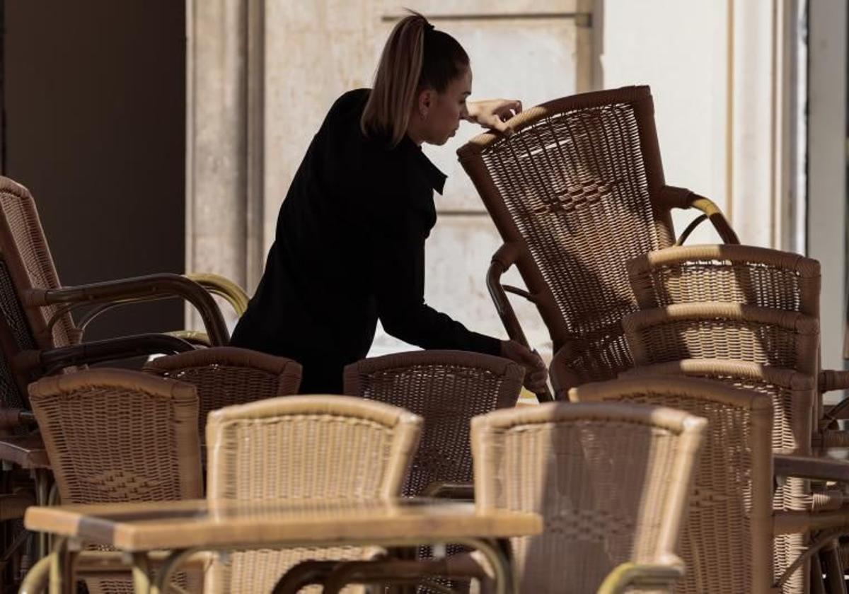 Una camarera apila las sillas en la terraza de un restaurante.