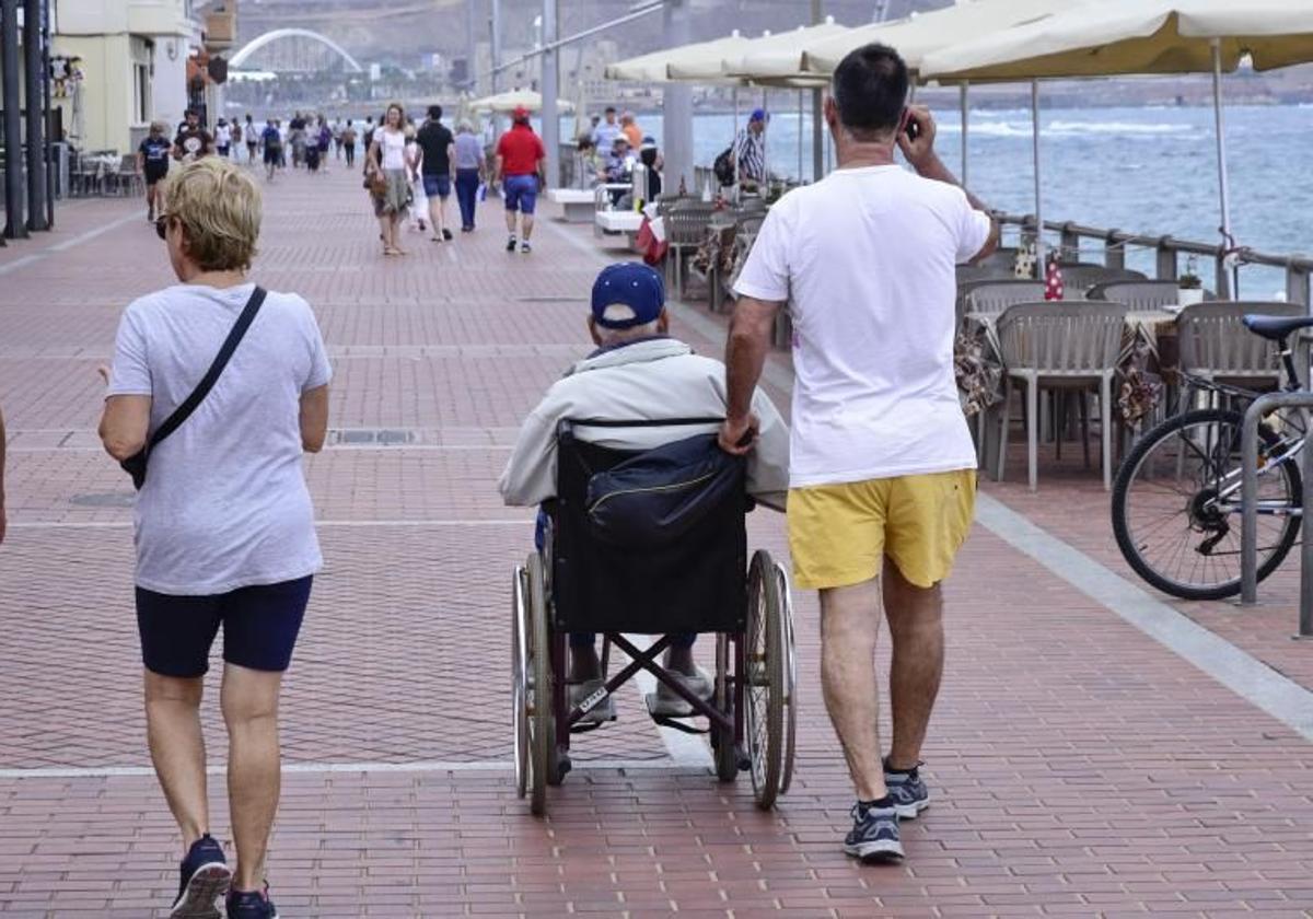Un hombre camina junto a una persona dependiente por el paseo de Las Canteras.