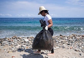 Una mujer con una bolsa de basura recogida en una playa.