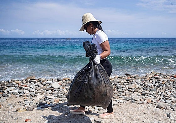 Una mujer con una bolsa de basura recogida en una playa.