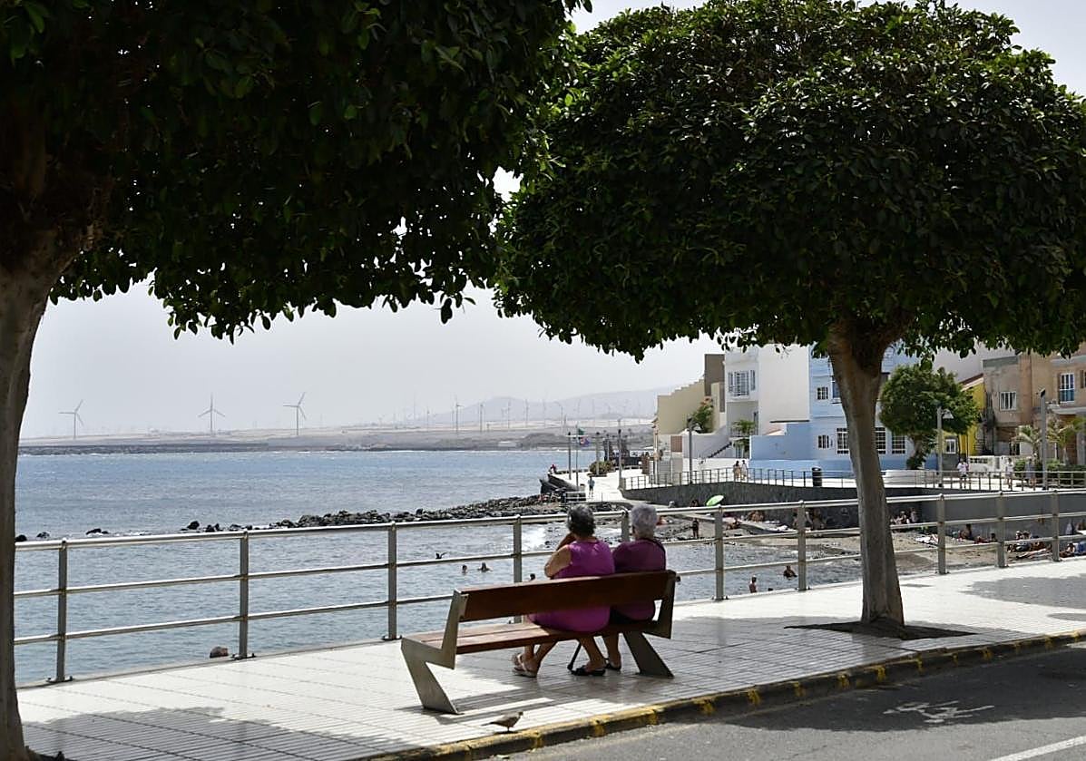 Dos personas sentada en el trozo a la sombra de un banco de Playa de Arinaga.