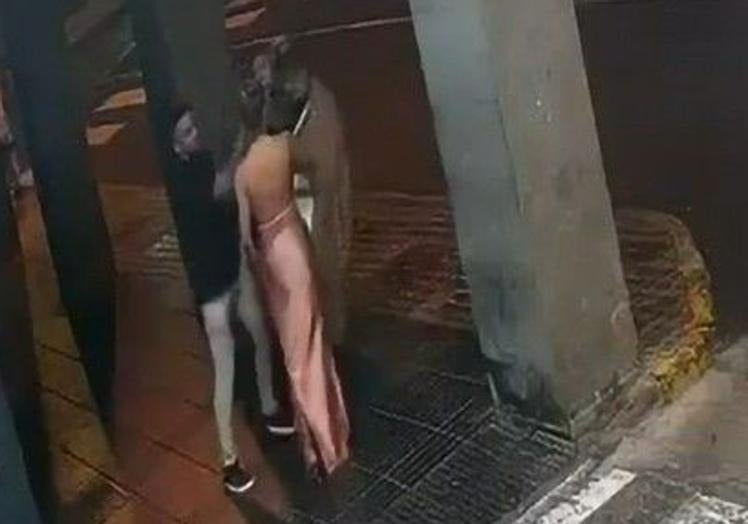 K. S. J. –de negro– empuja a Ortiz –con una chaqueta marrón–, en presencia de C. G. T., que va con un vestido rosa.