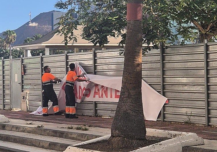 Operarios municipales retiran una de la pancarta que se colocó en el vallado de la obra.
