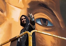 Dailos Socorro subido a un elevador mientras pinta el primero de los murales.