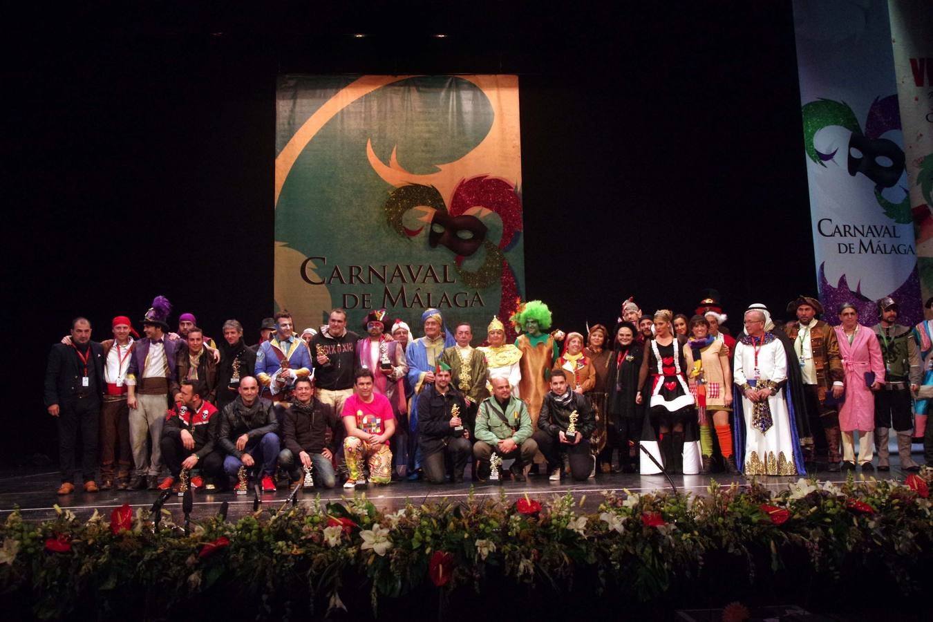 Foto de familia de los representantes de los grupos participantes en la final del carnaval con sus respectivos trofeos.