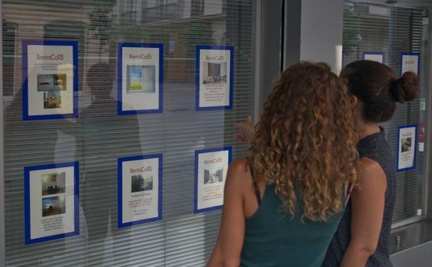 Clientas observan la oferta de viviendas de alquiler en el escaparate de la agencia Rentacasa. 