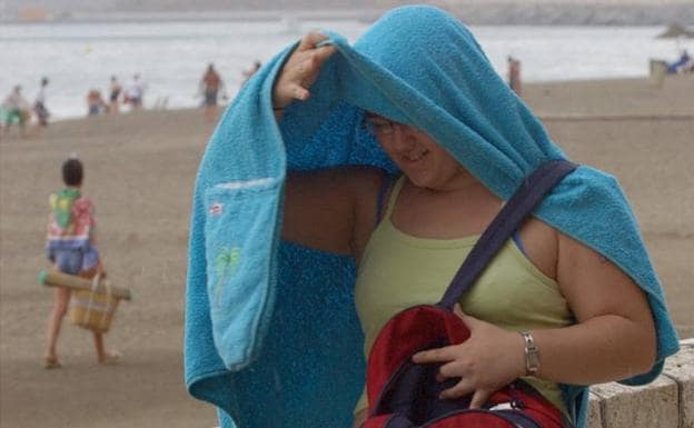 Una bañista se protege de la lluvia junto a la playa.