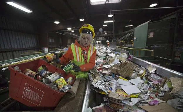Una operaria de una planta estadounidense de tratamiento de residuos clasifica la basura que corre por una cinta transportadora.