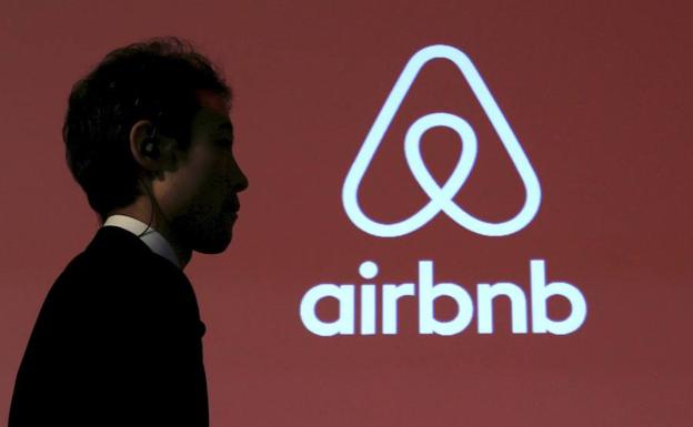 Un hombre camina junto a un logosímbolo de Airbnb. 