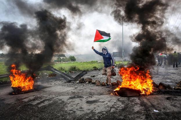 Un joven enarbola la bandera palestina en una de las barricadas incendiarias levantadas en las inmediaciones de uno de los accesos a la Franja de Gaza. :: A. Badarneh / efe
