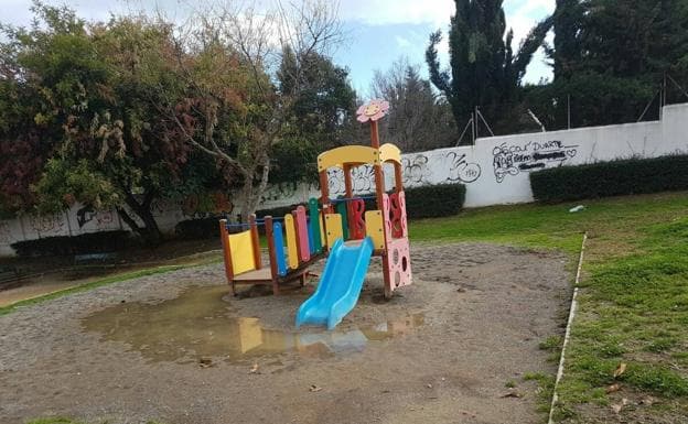 Imagen principal - El parque infantil se encharca en cuanto llueve y en él hay cacas. Un peatón cruza por el paso. La pintura apenas se ve.