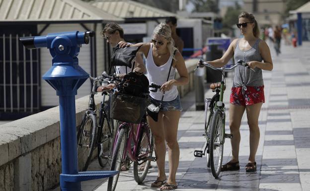 Turistas disfrutan del buen tiempo en un recorrido en bicicleta por el paseo marítimo.