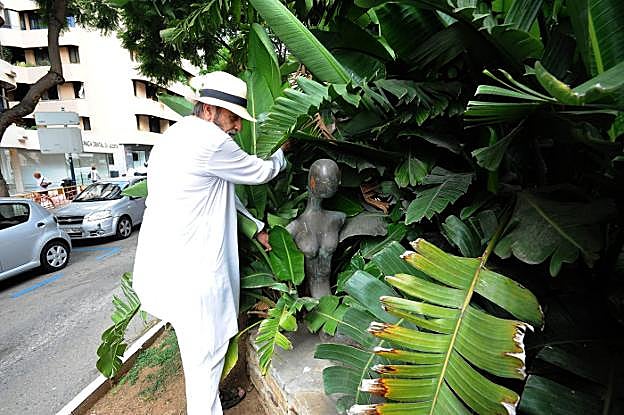 El artista Ramón Aymerich desplaza las ramas del palmeral para mostrar la escultura oculta. 