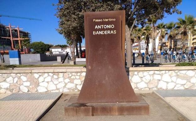 Monolito a la entrada del paseo marítimo Antonio Banderas, con un parterre seco y descuidado. 