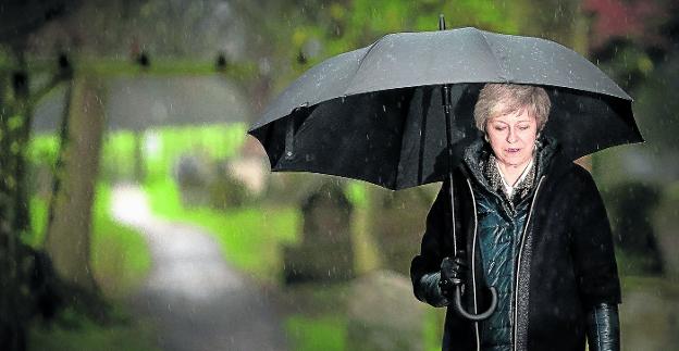 La primera ministra británica, Theresa May, se resguarda de la lluvia tras asistir, ayer, a un servicio religioso en Maidenhead, al oeste de Londres. :: Daniel LEAL-OLIVAS/ AFP
