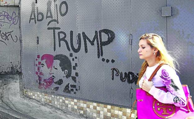 Una joven camina por una calle de Caracas en la que se observan pintadas a favor del régimen venezolano y en contra de Trump.