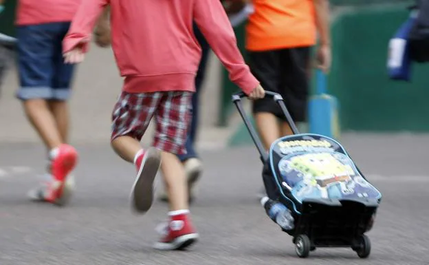 Un niño corre hacia el colegio llevando un carrito escolar. 