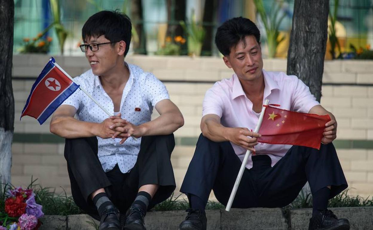 Dos hombres sostienen las banderas de China y Corea del Norte, mientras esperan la llegada del séquito oficial con los los mandatarios de ambos países en una plaza de Pyongyang.