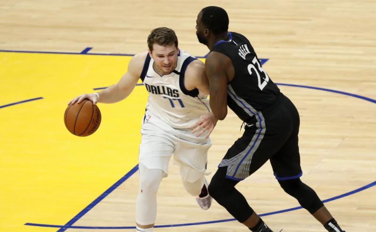 Luka Doncic trata de zafarse de Draymond Green. 