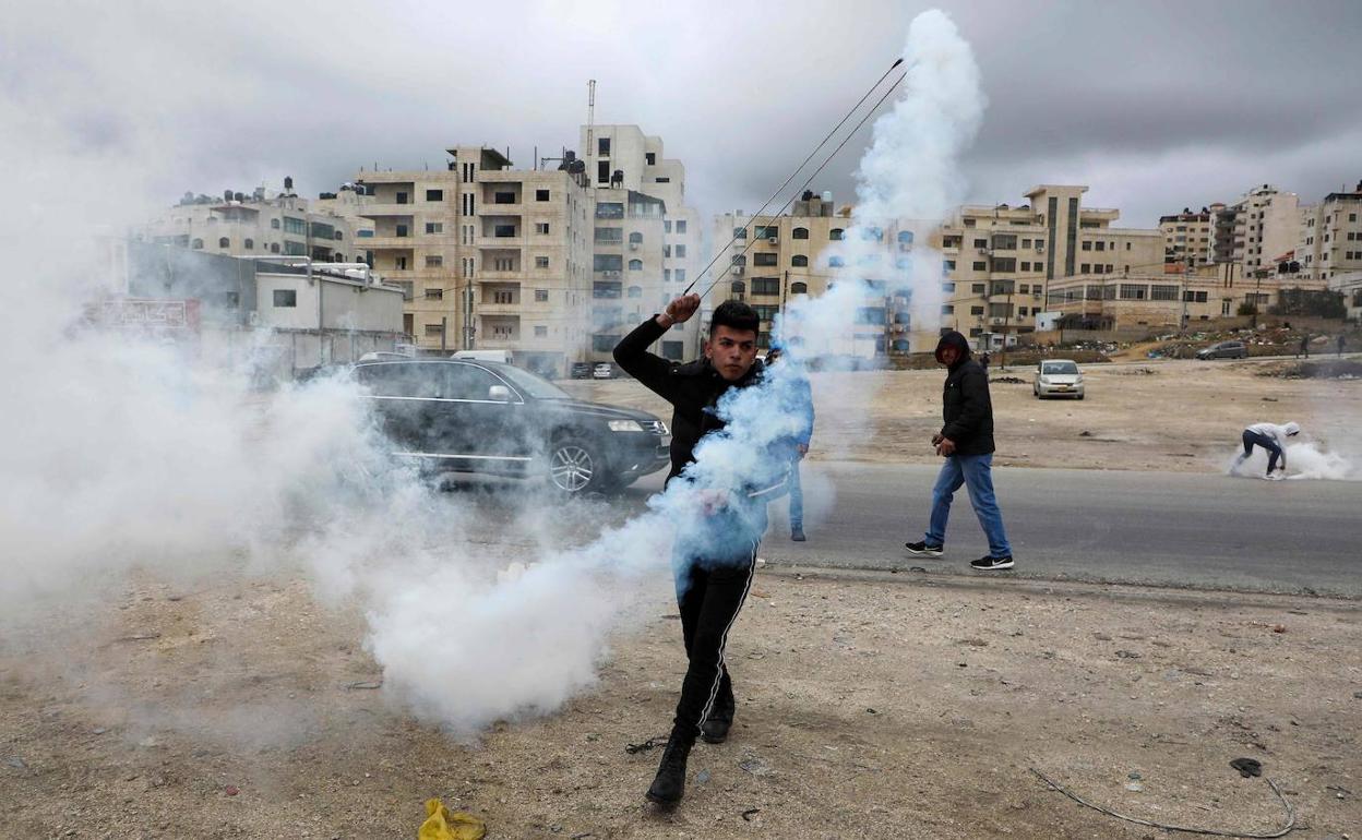 Un manifestante palestino lanza un bote de gas lacrimógeno contra las fuerzas de seguridad israelíes.